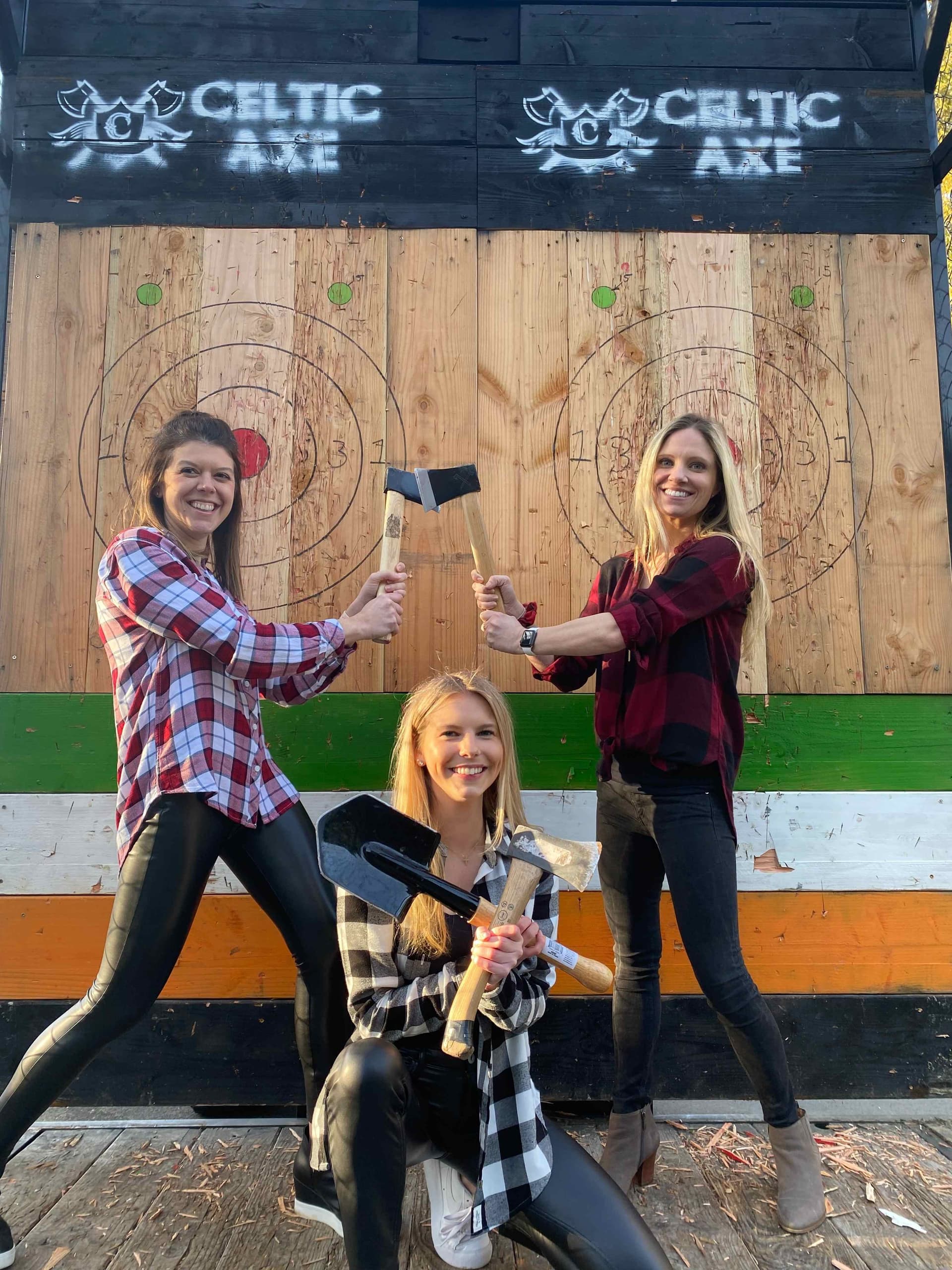 Three women in flannel shirts posing with axes at Celtic Axe