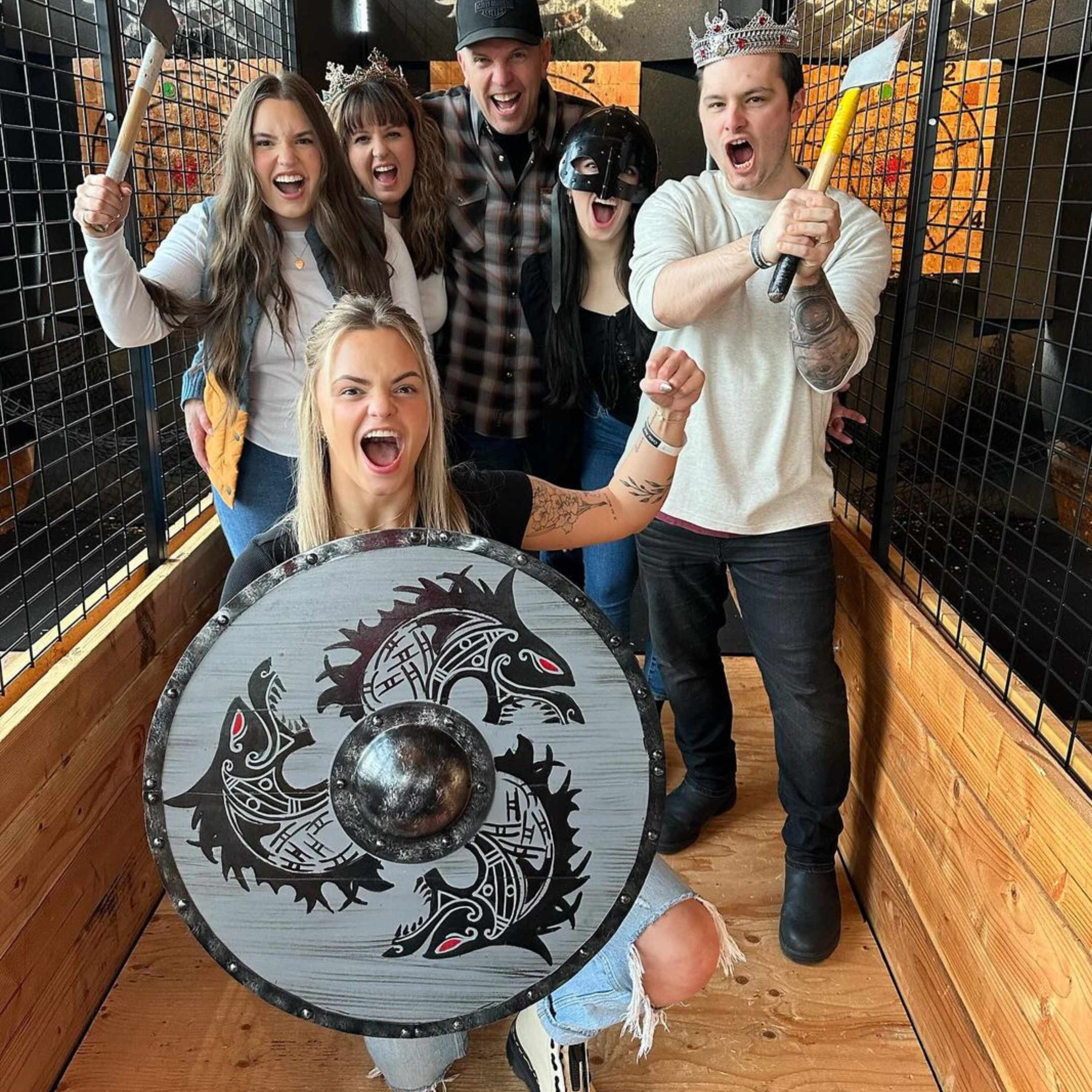 Group of guests celebrating with axes and a Viking shield in an axe-throwing lane